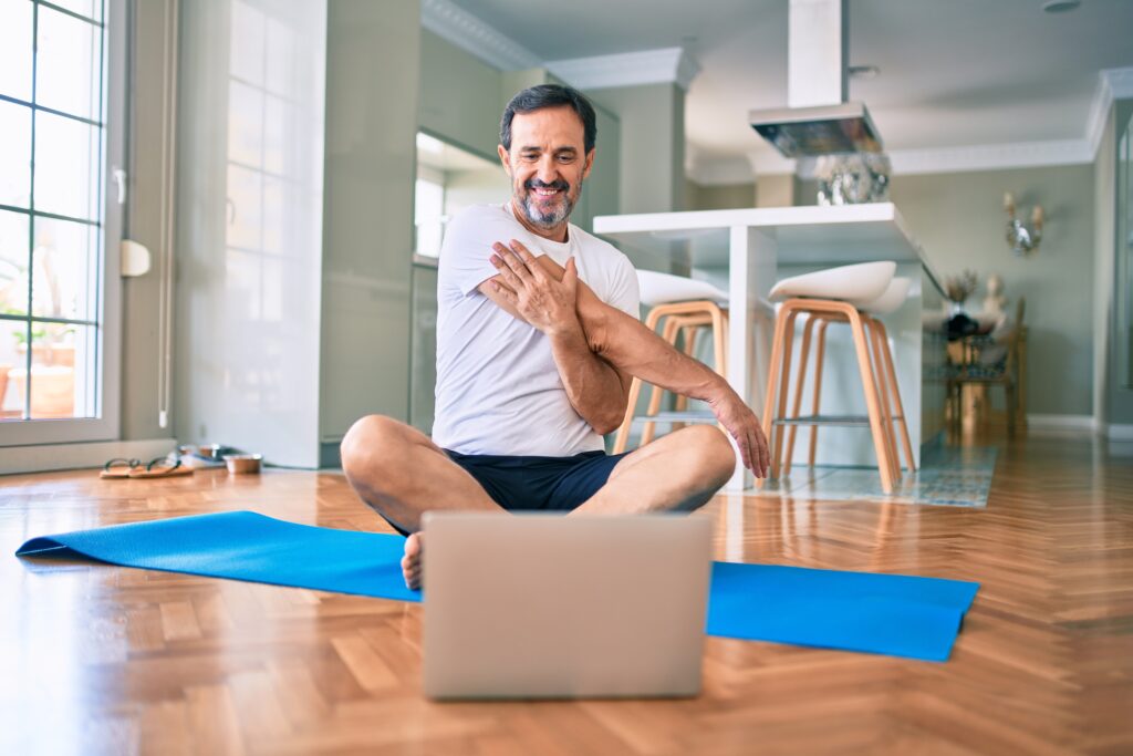 a man sitting on a yoga mat and participating in a virtual personal training session